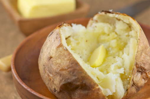 Baked potato with melted butter and freshly ground pepper in wooden bowl