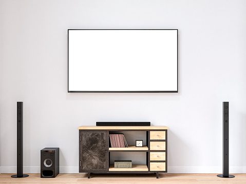 Modern living room with a blank (with white blank screen for copy space) LCD TV mounted on the white wall background, an industrial hardwood and black low cabinet with drawers under the TV and decorations (books, a clock, steel box), a TV surround sound system (with speakers, a loudspeaker, amplifier)  on the empty hardwood floor. 3D rendered image.