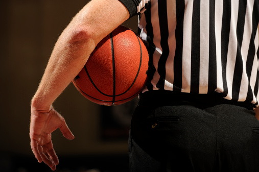 A Referee holds a basketball under his arm during a timeout.
