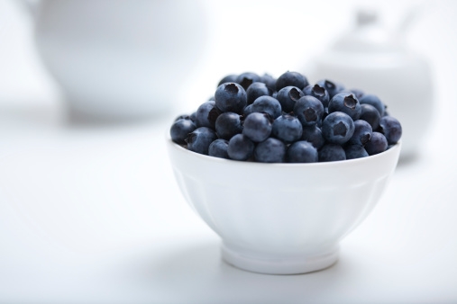 Heap of fresh blueberries in a white bowl with white objects in a white background with available copy space.