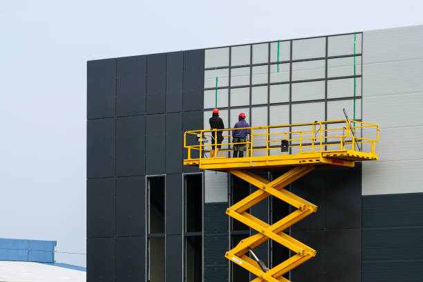 Large elevated aerial scissor lift working platform with workers against grey sandwich panels wall Large yellow elevated aerial scissor lift working platform with workers at grey new industrial building sandwich panels wall, industrial lifter sandwich panel photos stock pictures, royalty-free photos & images