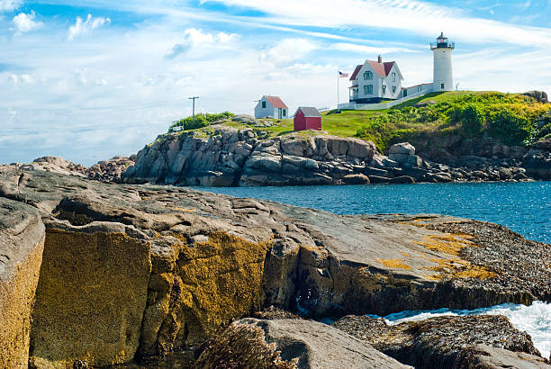 The Nubble Lighthouse at Cape Neddick located on the coast of Maine with rocky terrain in the foreground.