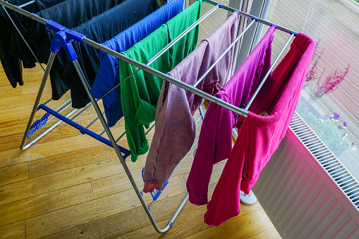 Drying in the apartment, colorful clean clothes hanging on drying rack next to a white heating radiator, indoor excessive humidity problem