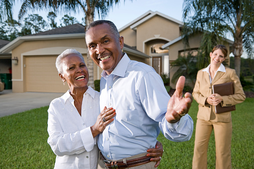 African American couple with real estate agent outside house in front yard