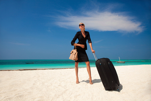 Business woman standing on beach with suitcase