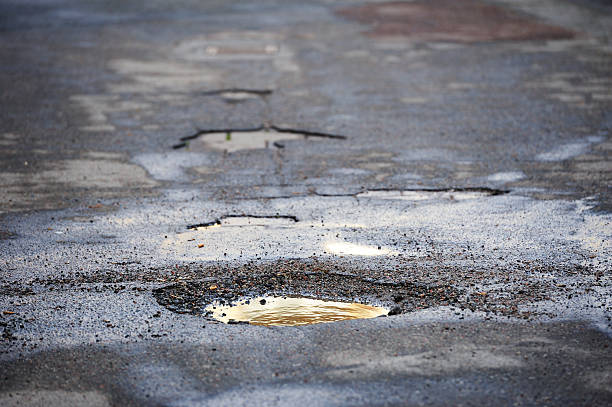 Pot hole on asphalt road "Low sun, old road, puddle reflecting sunlight after rain." dirt hole stock pictures, royalty-free photos & images