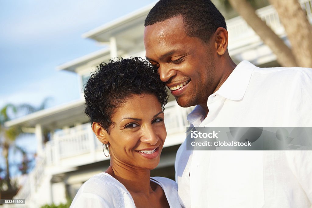 Coppia sorridente con la loro casa in background - Foto stock royalty-free di Abbigliamento casual