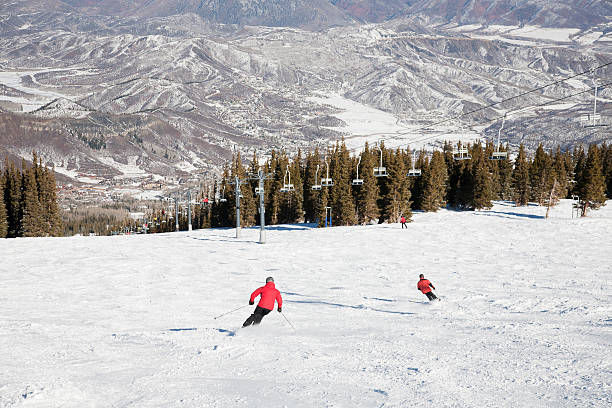 Skiers on a steep slope dropping into a valley with small town below