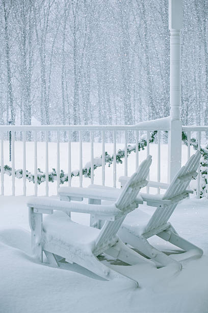 Adirondack chairs on a porch on a snowy day. Christmas roping is draped across the railing.