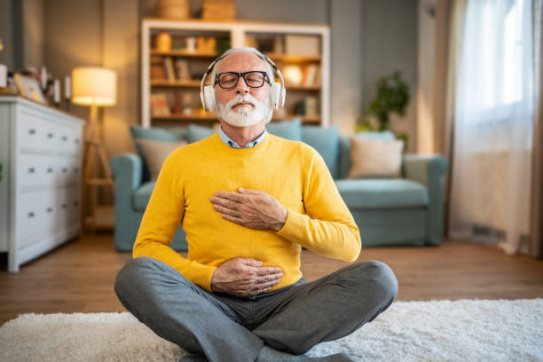 istock Elderly man, pensioner, sitting on floor practicing guided meditation at home, relaxing body and mind concept 1833659643