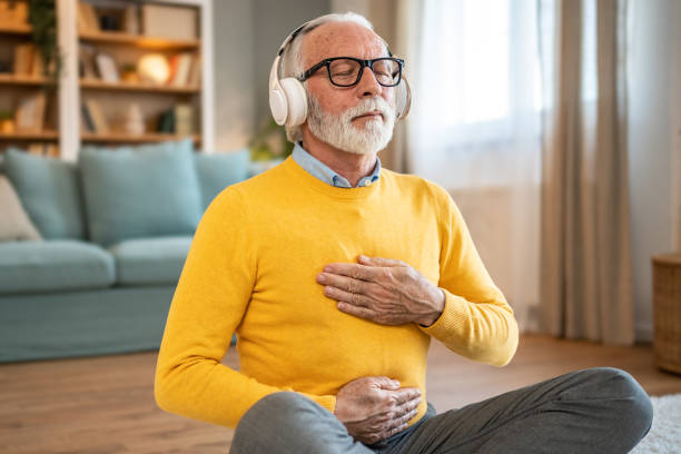 istock Elderly man, pensioner, sitting on floor practicing guided meditation at home, relaxing body and mind concept 1833659648