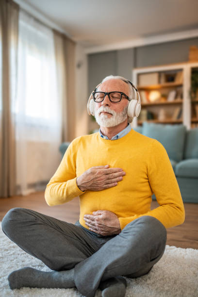 istock Elderly man, pensioner, sitting on floor practicing guided meditation at home, relaxing body and mind concept 1833659664