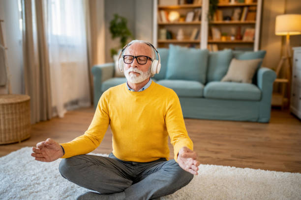 istock Elderly man, pensioner, sitting on floor practicing guided meditation at home, relaxing body and mind concept 1833660763