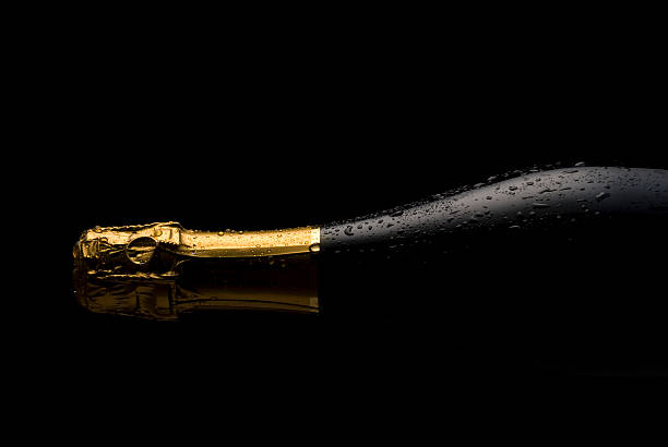 Cold Champagne bottle A studio shot of a cold Champagne or sparkling wine bottle with a gold top and water droplets.The image is shot horizontally on a black background with low key lighting wine bottle photos stock pictures, royalty-free photos & images