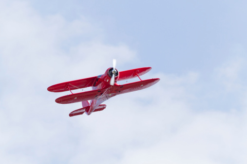 Red biplane with one propeller flying in a blue sky. Shot from below / front.