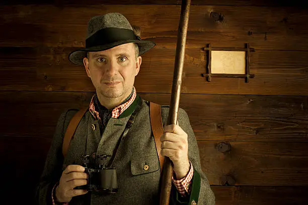 Austrian style ranger in traditional costume with walking sticks and binoculars in front of a wooden background. With empty picture frame for own text/picture.Maybe you like also one of these: