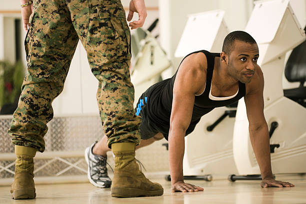 Trainee Doing Burpees at a Fitness Bootcamp Bootcamp fitness trainer standing over trainee as he does Burpees a full body workout exercise. Horizontal shot. military camp stock pictures, royalty-free photos & images