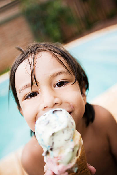 A portrait of a young boy eating ice cream by a poolside stock photo