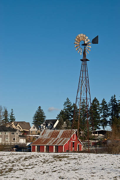 Red Barn, Windmill and Housing Development This well preserved barn is said to be over 100 years old. Here it is shown on a cold winter day with a housing development as a backdrop. The historic barn sits on a small farm in Edgewood, Washington State, USA. jeff goulden barn stock pictures, royalty-free photos & images