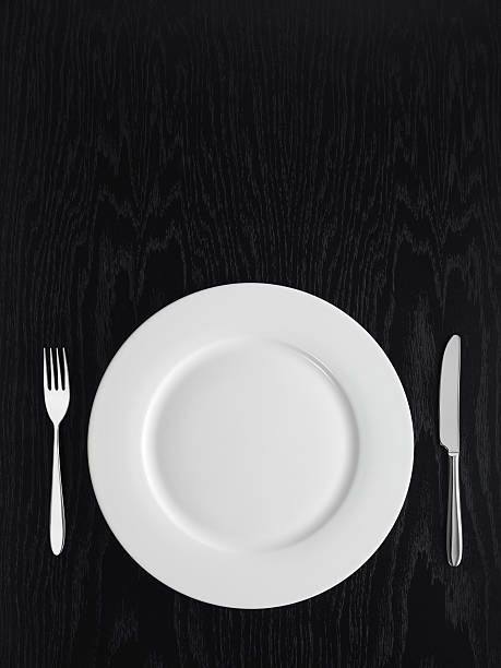 A white plate, a knife and a fork on a black table. Directly above view of table setting on a black table garden fork stock pictures, royalty-free photos & images