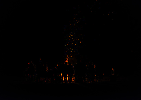 A campfire's flames and sparks can be seen in the darkness of night
