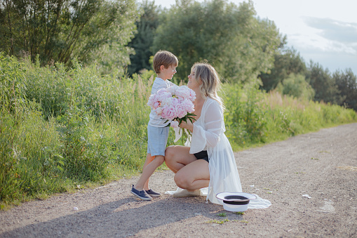 Mom and son. Preschooler boy congratulates his mother on her birthday, givesbouquet of peonies .