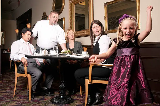 A little girl is acting up in a restaurant while diners look on.