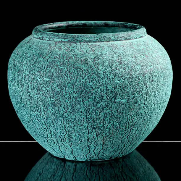 A metal vase with an oxidised copper finish reflected in glass.