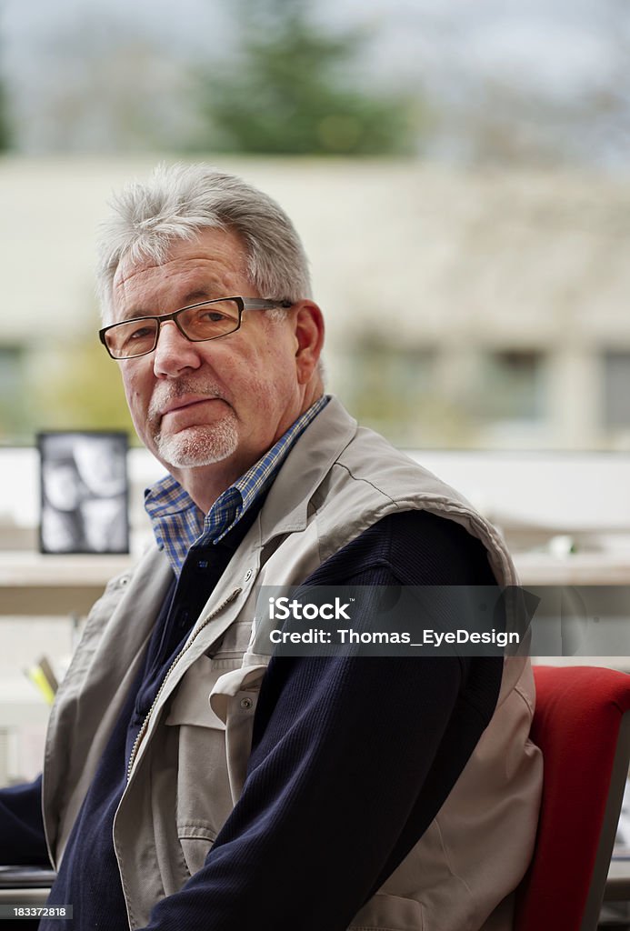 Senior Man at an Office Desk Senior business owner looks towards the camera while seated at his office desk. Vertical shot. 60-64 Years Stock Photo