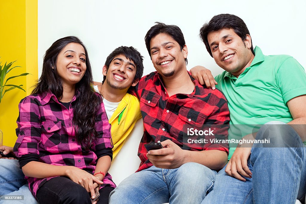 Quatro jovens amigos alegres indiano com telefone celular no sofá - Foto de stock de 20 Anos royalty-free