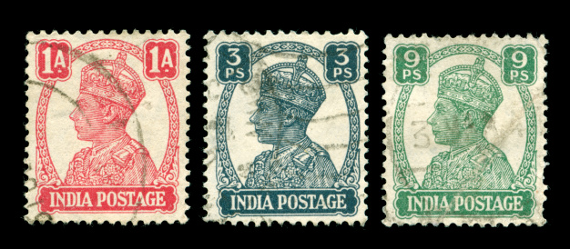 Portrait of King George VI on red, blue and green Indian stamps from 1943, scanned on black background.