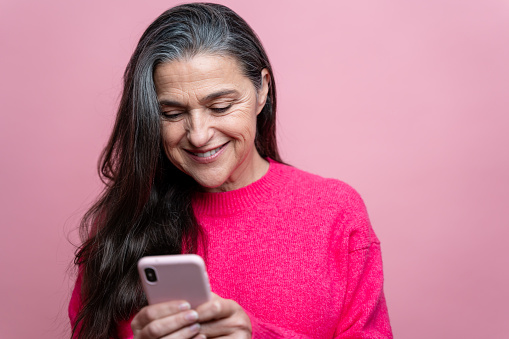 Portrait of a happy senior woman using mobile phone against pink background
