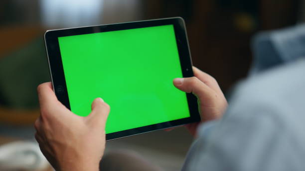 istock Gamer hands playing mockup tablet at room. Closeup man tapping greenscreen pad 1833756929