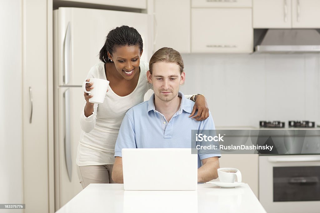 Drink coffee and read news in the morning. "Young couple reading internet news on laptop in white/beige kitchen, drinking coffee in the morning.Similar images preview:" 20-24 Years Stock Photo