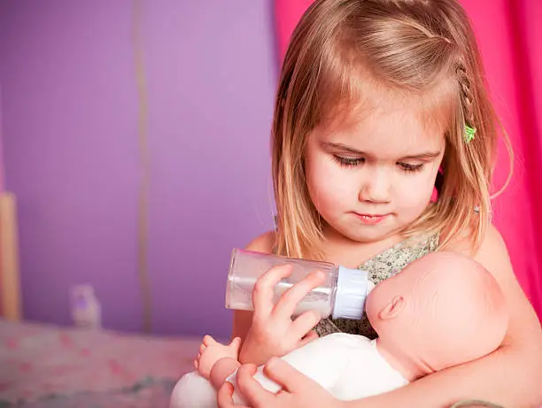 Color image of a little girl holding her baby while feeding her.