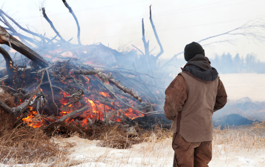 Farmer keeping an eye on a burning brush pile in a snowy field. For more farming images...