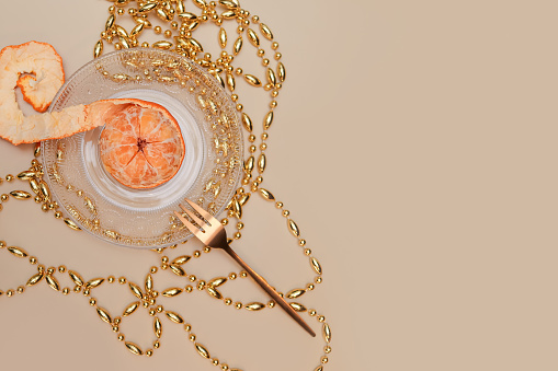 tangerine with peeled peel on a plate decorated with gold festive beads and fork. copy space, top view, flat lay