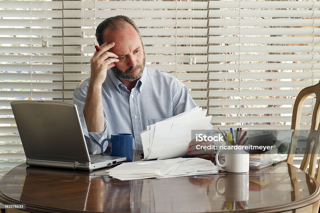 Middle Aged Male Homeowner Struggles With Paying Bills Debt Unemployment This middle age male sits at the kitchen table frustrated with stack of bills to pay and mounting debt. Owner Stock Photo