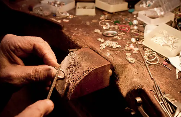 An old jeweler making a white gold ring in his studio. Similar working hands concept below