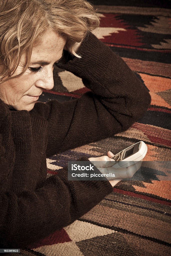 Mature Woman Writing Sms On The Phone "Mature woman (56s) writing sms on the phone, lying on the carpet." 55-59 Years Stock Photo