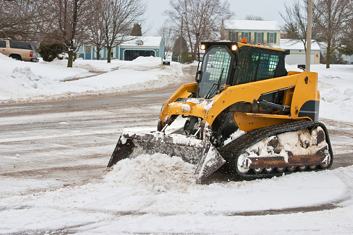 a small tracked type vehicle with a front end loader cleans up the snow in a suburban cul de sac after a storml near chicago IL