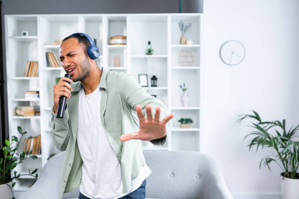 istock Carefree Singer. Cheerful young guy singing favorite song using remote control as microphone, dancing wearing wireless headset. Excited man having fun at home 1833831500