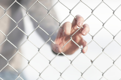 One hand gripping chain link fence.Focus is on hand near fence
