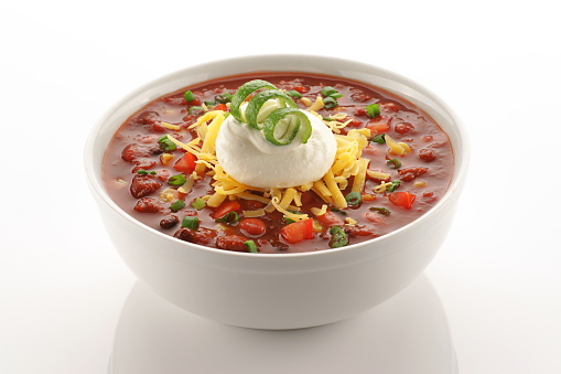 Bowl of vegetarian chili garnished with cheese, sour cream and a lime twist on clean white.