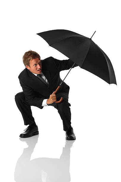 Photo of Businessman crouched down shielding himself with an umbrella