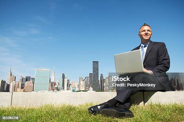 Sonriente Hombre De Negocios Sentado Con Ordenador Portátil Al Aire Libre Con Vista A La Ciudad Foto de stock y más banco de imágenes de Ordenador portátil