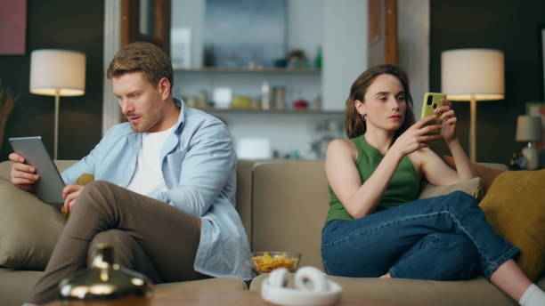 istock Involved couple reading devices at room. Internet addicted family using gadgets 1833867874