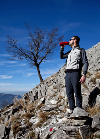 vertical shot of an young hiker drinking from a red water bottle