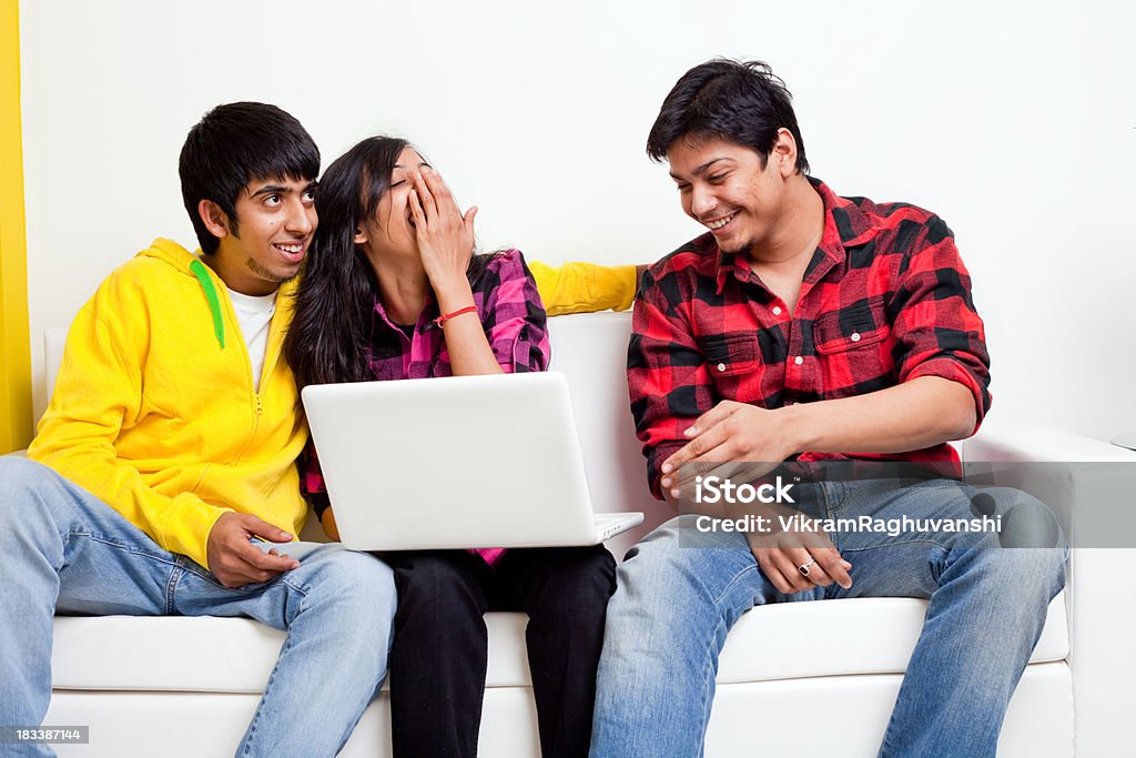 Three Young Indian Alegre amigos con una computadora portátil en el sofá de la sala de estar con sofá - Foto de stock de 20 a 29 años libre de derechos
