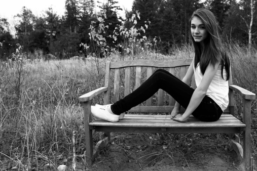 A portrait of a beautiful teenage girl sitting on a bench outside.